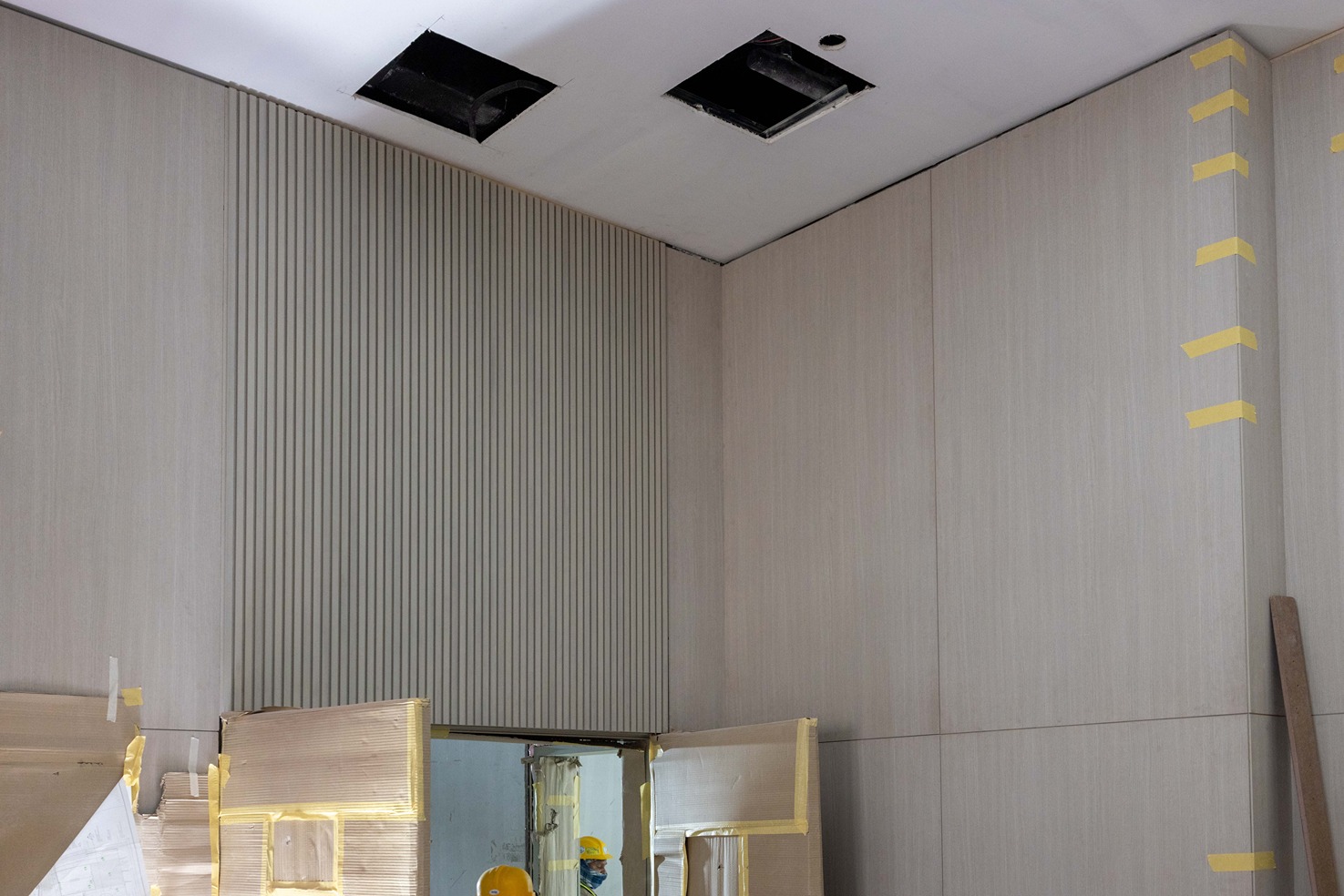 Pearl House By Imtiaz An unfinished room with gray paneling, exposed ceiling sections, and yellow tape indicating construction work.
